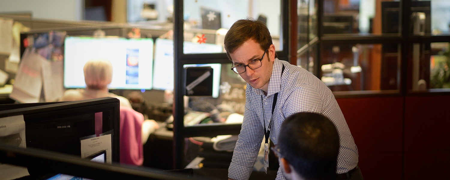 Tyler Dukes talks to a coworker in the newsroom