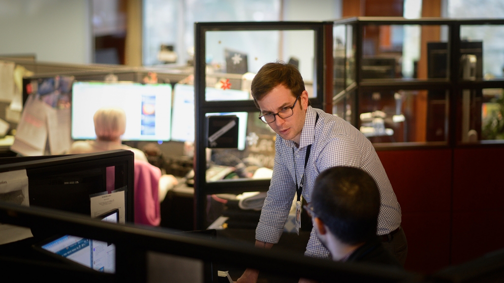 Tyler Dukes talks to a coworker in the newsroom