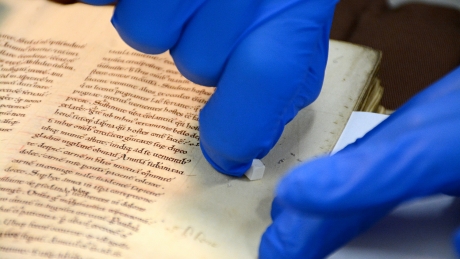 Wearing blue goves, English professor Tim Stinson rubs a plastic eraser against a manuscript.