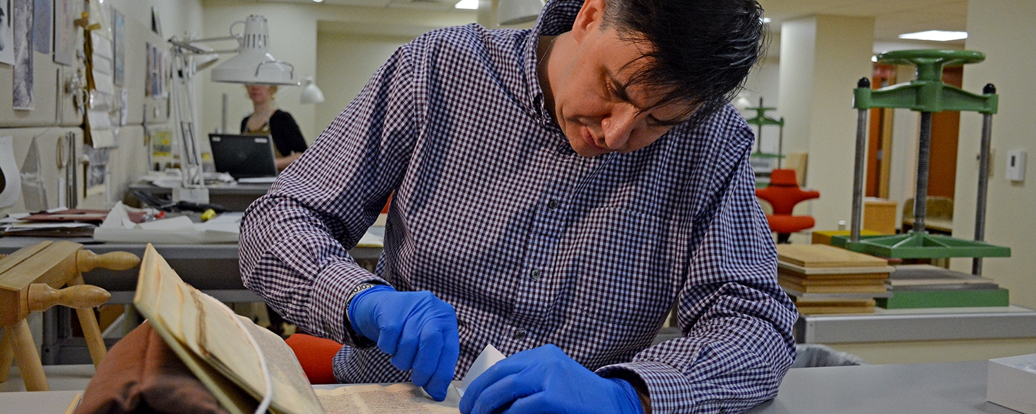 Wearing blue gloves, Tim Stinson rubs a plastic eraser against an old manuscript.