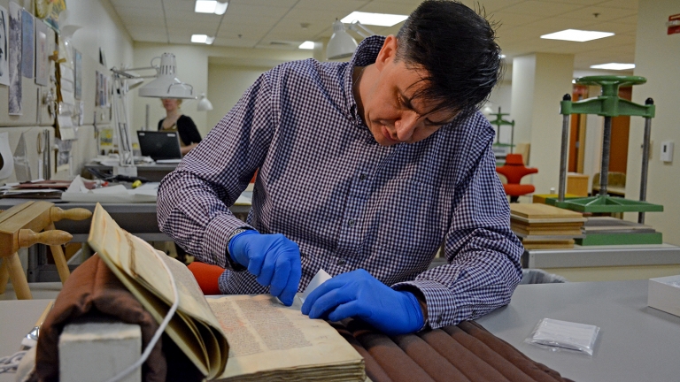 Wearing blue gloves, Tim Stinson rubs a plastic eraser against an old manuscript.