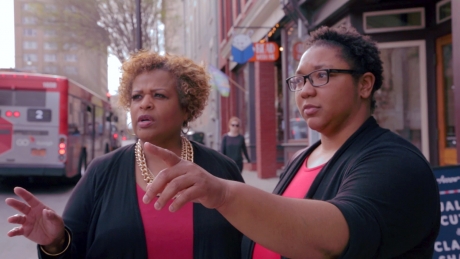 Lisa Withers and Sylvia West stand on Hargett Street in downtown Raleigh, pointing at a building.