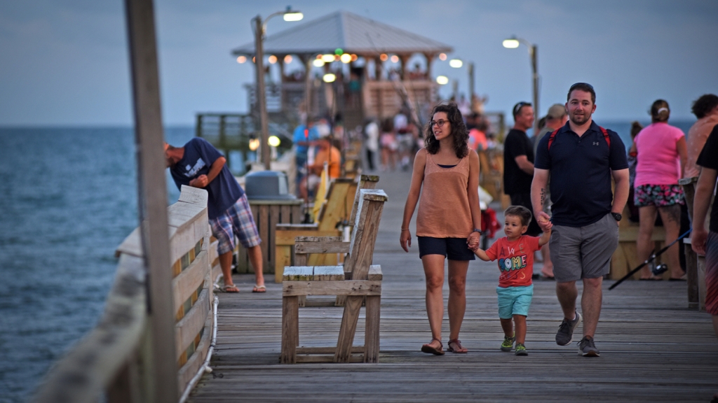 People walk down a fishing pier along the ocean.