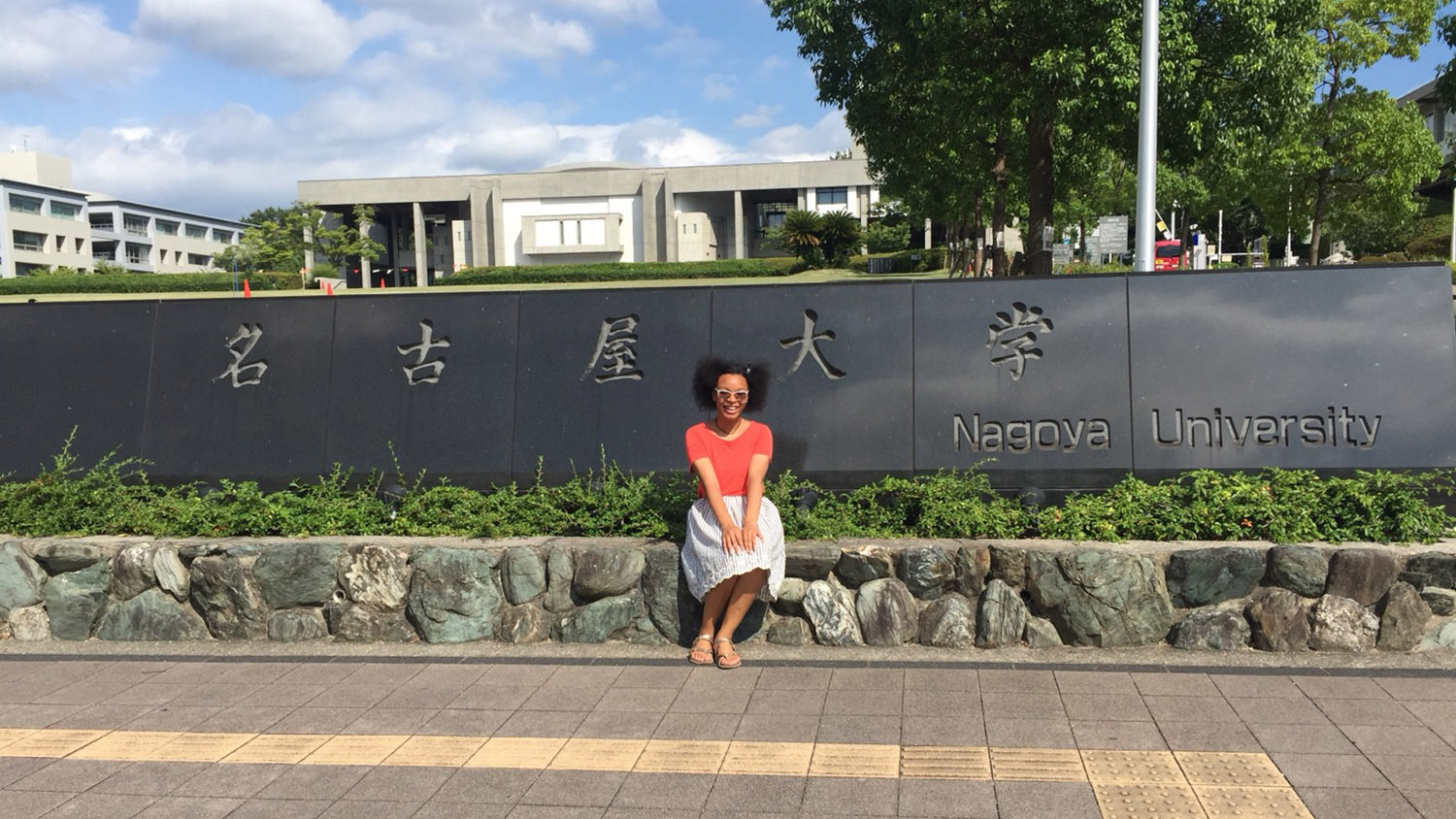 student sitting in front of Nagoya University sign