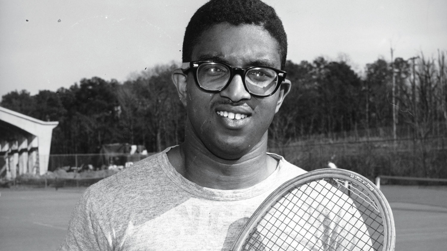 A black and white photo of Irwin Holmes, one of the first African American undergraduate students at NC State, standing with a tennis racket.