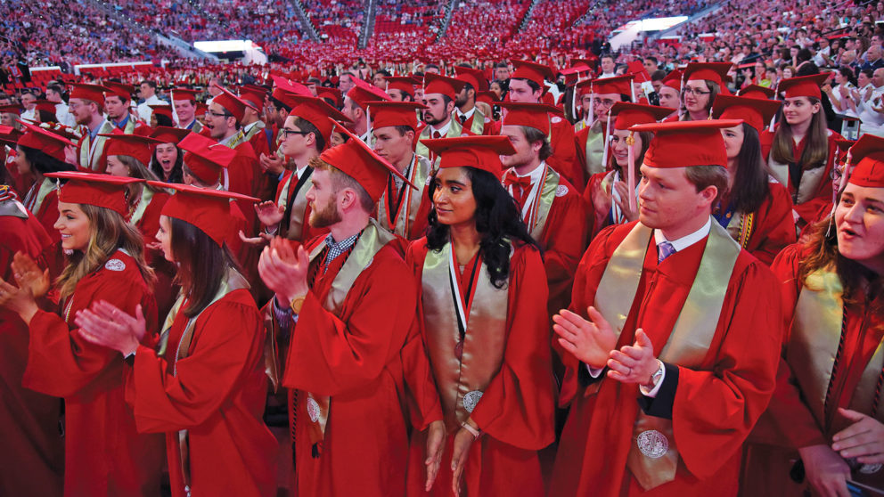 Students in red robes clap during their graduation ceremony on NC State's campus.