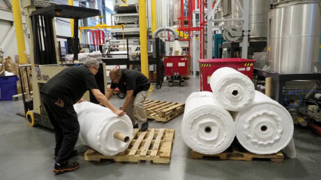 Two men in a warehouse handle rolls of innovative spunbond filtration material.